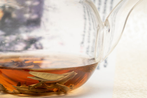 Load image into Gallery viewer, Jasmine Silver Needle tea steeping in a glass teapot, showcasing delicate silver needle leaves and rich amber infusion.