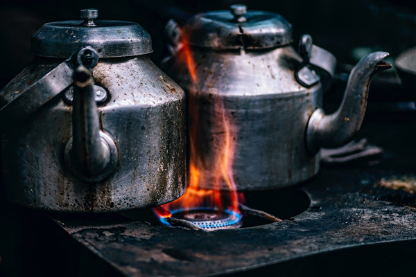 Two metal kettles boiling on a stove with flames, creating a warm, inviting atmosphere in a kitchen.