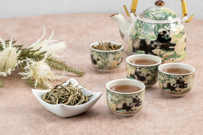 Jasmine Silver Needle tea served in decorative cups with a matching teapot and leaves on a table.